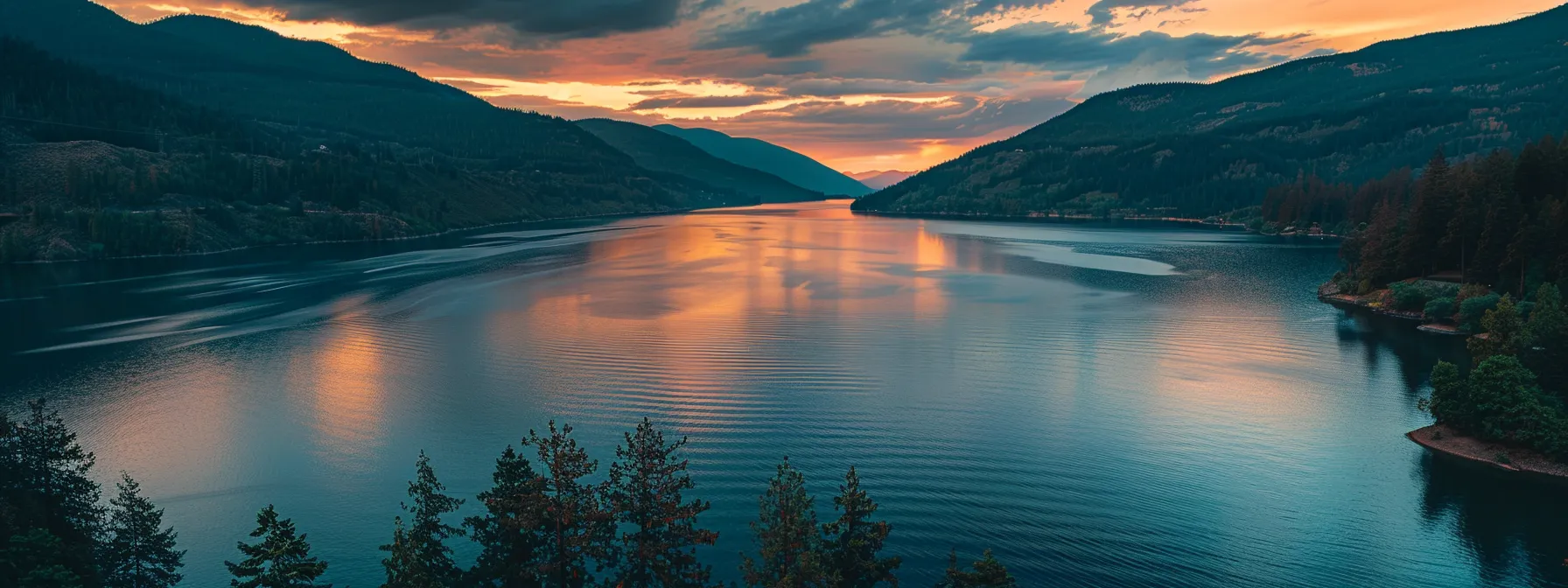 ein atemberaubender sonnenuntergang über einem ruhigen see, dessen spiegelglattes wasser die leuchtenden farben des himmels reflektiert und die umrisse üppiger bäume am ufer sanft umschmeichelt.